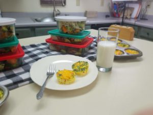 Omelet muffins on a plate beside a glass of milk and stacked meal prep containers behind the plate of muffins